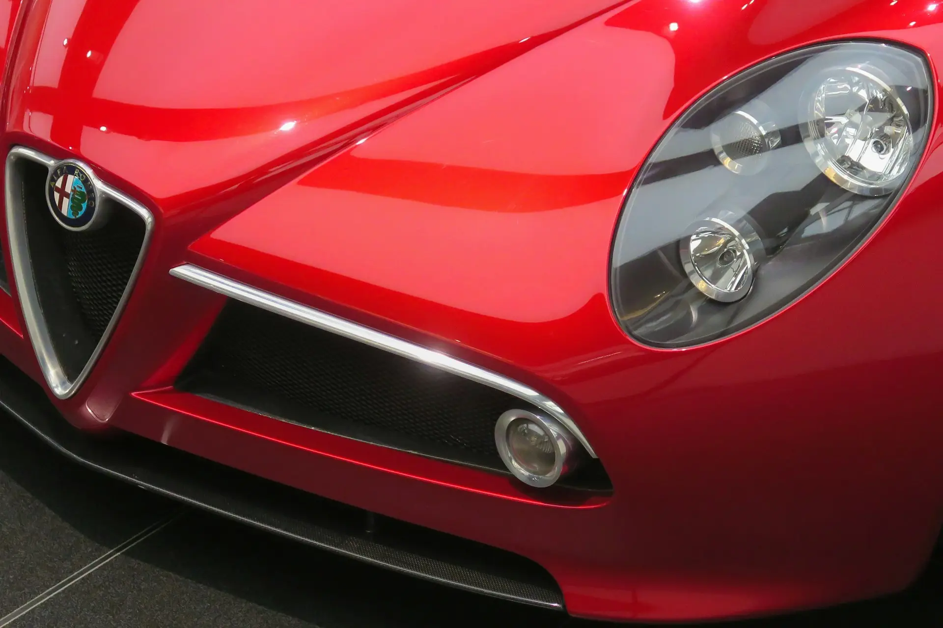 Red Alfa Romeo Sports Car Front Closeup Close-up view of the front of a shiny red Alfa Romeo sports car, highlighting the iconic grille, headlight, and emblem.