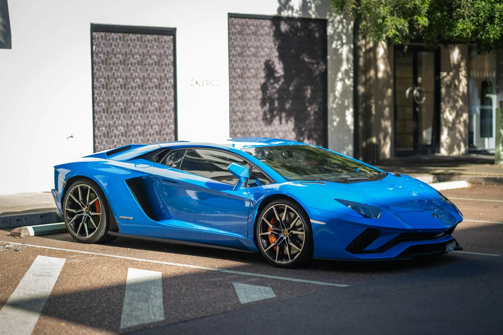 Blue Lamborghini Aventador Parked on Street A vibrant blue Lamborghini Aventador parked on a street, showcasing its sleek design and sporty wheels.
