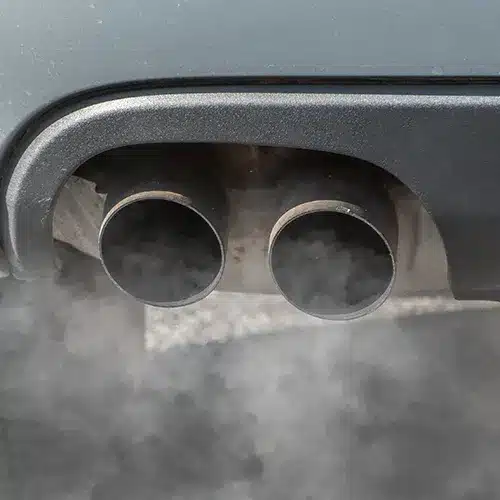 Car Exhaust Pipes Emitting Smoke Close-up of two car exhaust pipes releasing a plume of dark smoke.