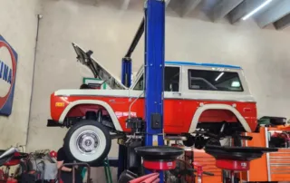 Classic Ford Bronco on Hydraulic Lift in Auto Shop Red and white early model Ford Bronco SUV on a blue hydraulic lift in a busy auto repair garage.
