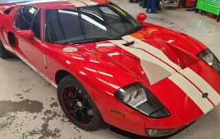 Red Ford GT Supercar in Garage with White Racing Stripes Red Ford GT sports car with white racing stripes, black wheels, parked in a garage with tools in background.
