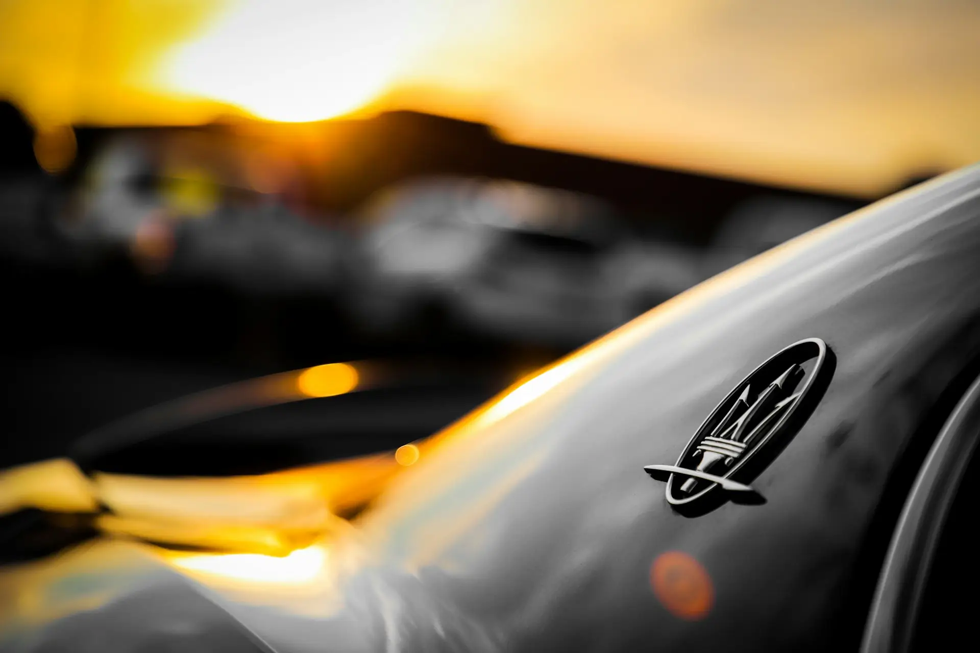 Maserati Trident Emblem Bathed in Golden Sunset Light Maserati trident logo on a sleek dark car's side panel, reflecting golden hour sunlight.