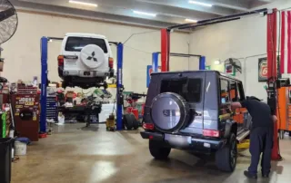 Car Repair Shop With Cars On Lifts Mechanic working on a black SUV in a car repair shop, with a white SUV lifted in the background.