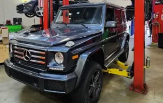 Mercedes Benz G550 on Car Lift for Service Dark gray Mercedes Benz G550 SUV elevated on a red car lift in a garage for maintenance.
