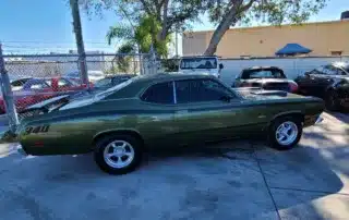 Classic Green Dodge Dart Muscle Car Parked Outdoors A classic green Dodge Dart muscle car with black racing stripes parked on a paved lot.