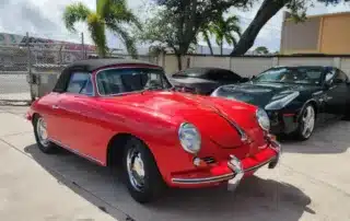 Red Convertible Classic Car and Dark Sports Cars A bright red classic convertible Porsche Speedster with a black top parked next to two dark sports cars, one black and one da