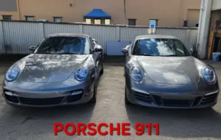 Two Porsche 911 Cars Parked Outside Building Two gray Porsche 911 cars parked side-by-side in front of a building with a fence.