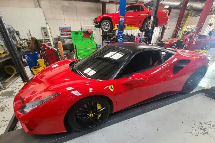 Red Ferrari Sports Car On Lift In Professional Auto Repair Shop Red Ferrari sports car with black roof on a hydraulic lift in a busy automotive repair garage