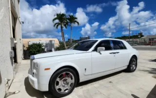 Luxury White Rolls-Royce Phantom Parked Outdoors A pristine white Rolls-Royce Phantom sedan parked on a paved surface under a partly cloudy sky.