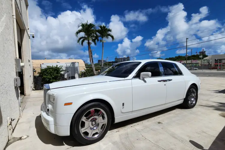 Luxury White Rolls-Royce Phantom Parked Outdoors A pristine white Rolls-Royce Phantom sedan parked on a paved surface under a partly cloudy sky.