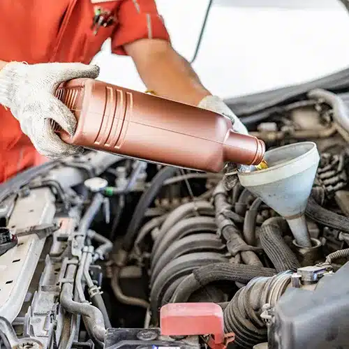 Mechanic Pouring Oil into Car Engine with Funnel Close-up of a mechanic in red overalls and white gloves pouring oil from a copper-colored bottle into a car engine via a funn